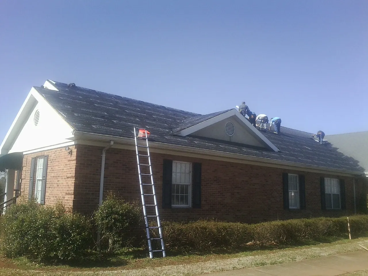 Crew tearing shingles off a brick ranch roof with a ladder set — Emergency Roof Repair work by our crew in Pitcairn