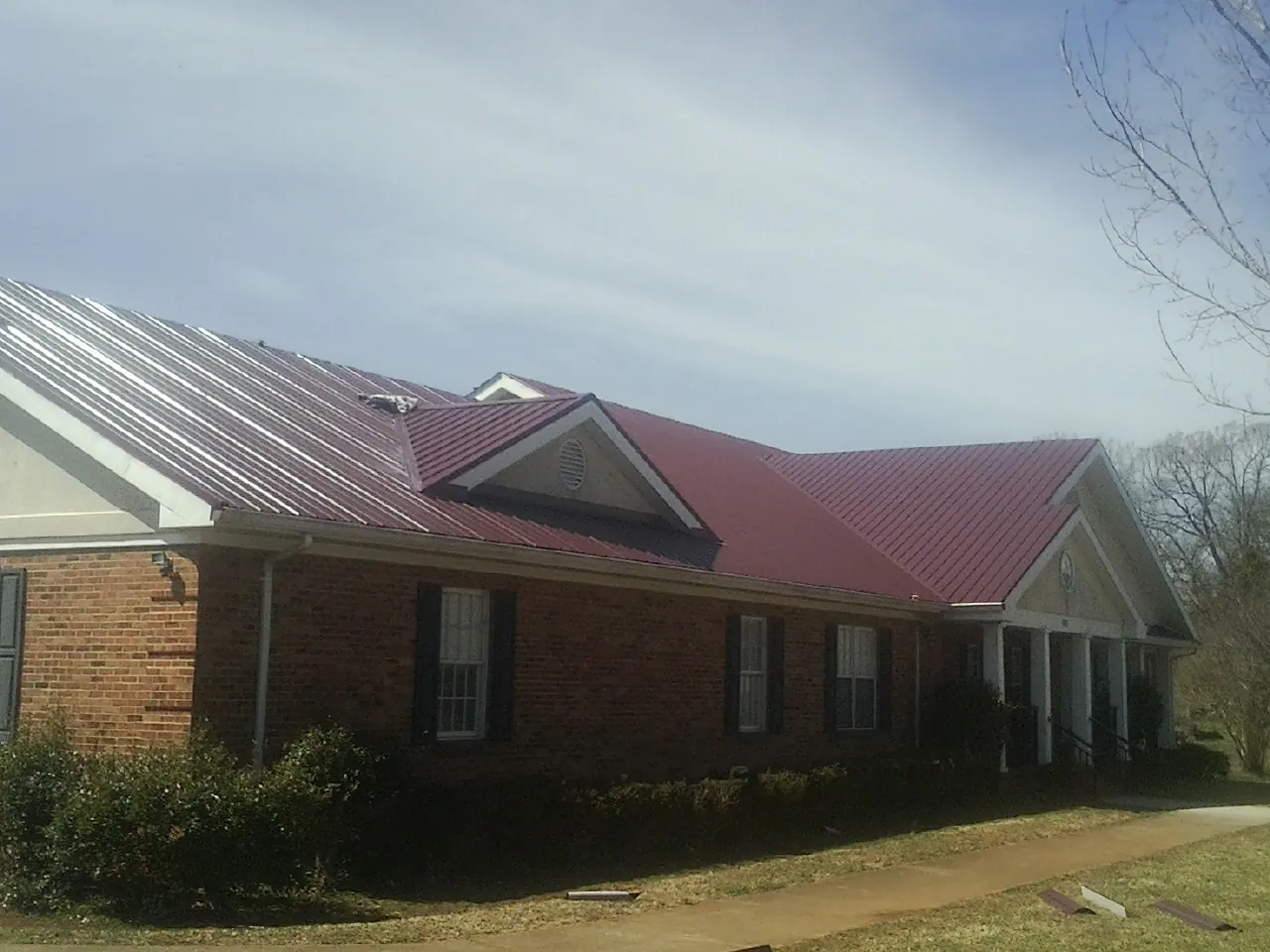 Red metal roof with gabled entries on a long brick building, from a Hail Damage Roof Repair job in Pitcairn