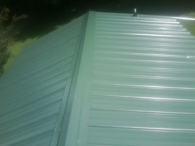 New green metal panels meeting at the ridge of a roof — Flat Roof Repair work by our crew in Pitcairn