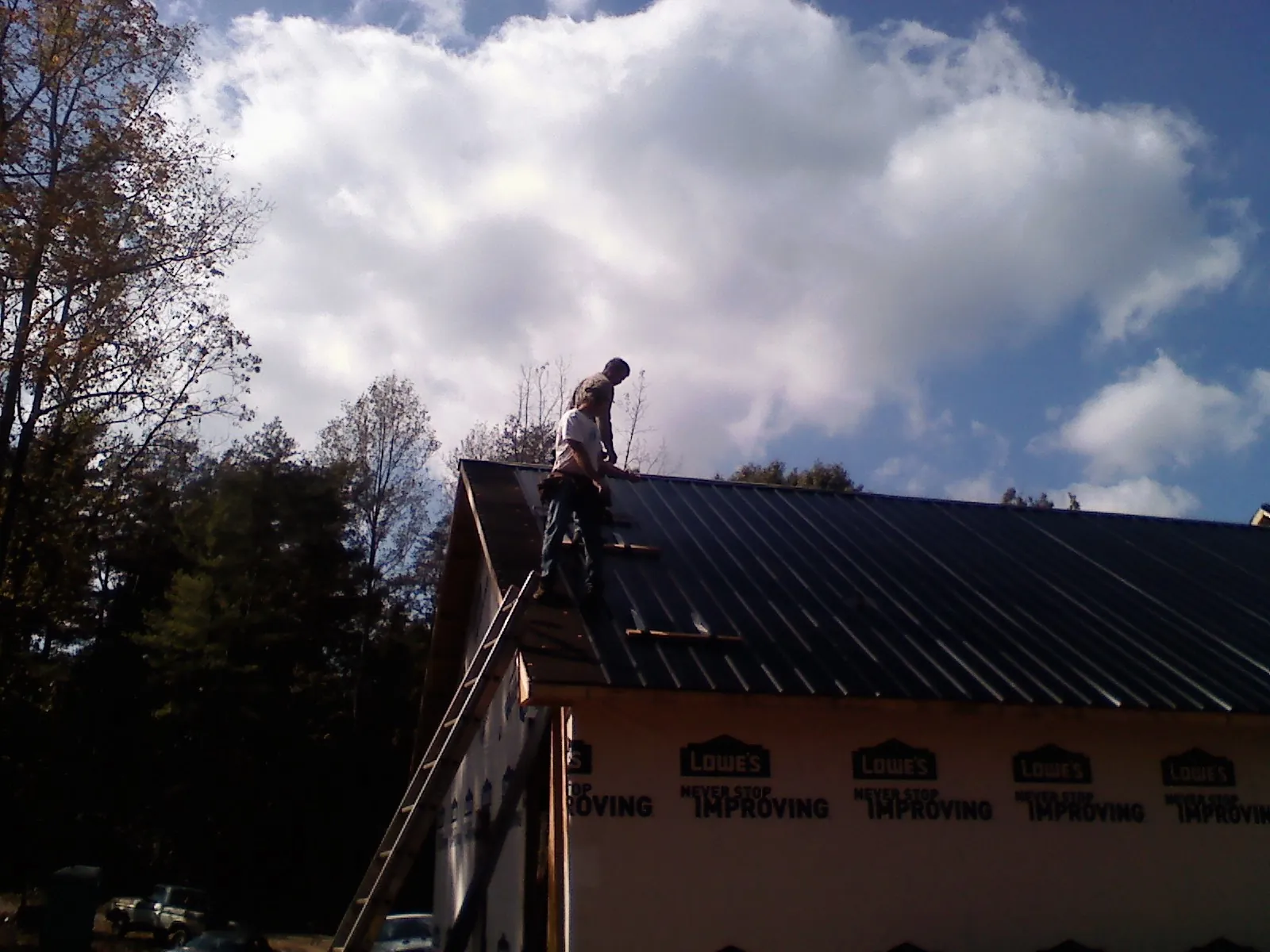 Roofer fastening dark metal panels high against a cloudy sky, from a Roof Inspection job in Pitcairn