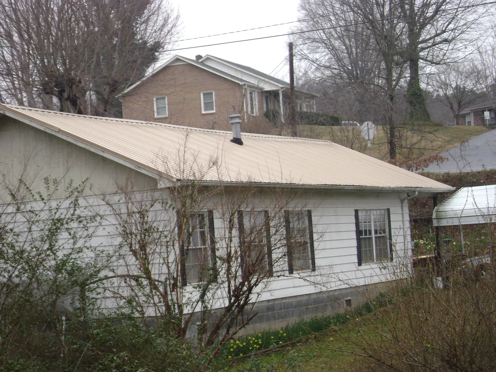 Tan metal roof on a white sided house set into a hillside — Commercial Roofing by Roofing Brothers in Pitcairn
